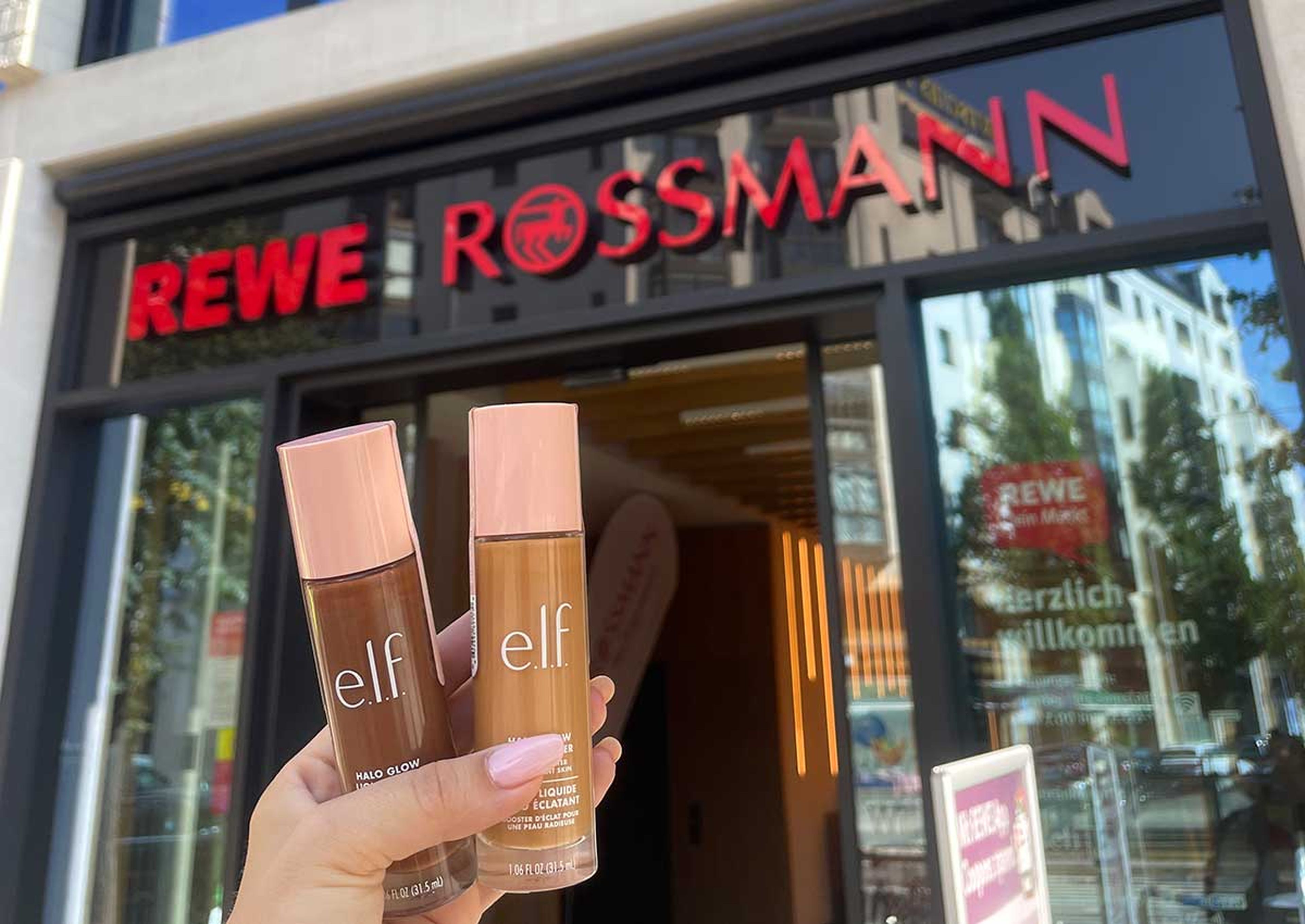 someone holding up elf products in front of a rewe rossmann storefront