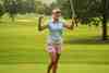 Golfer with both arms raised in celebration on a tree-lined fairway