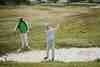 Golfer playing out of a bunker while a playing partner watches on a links course