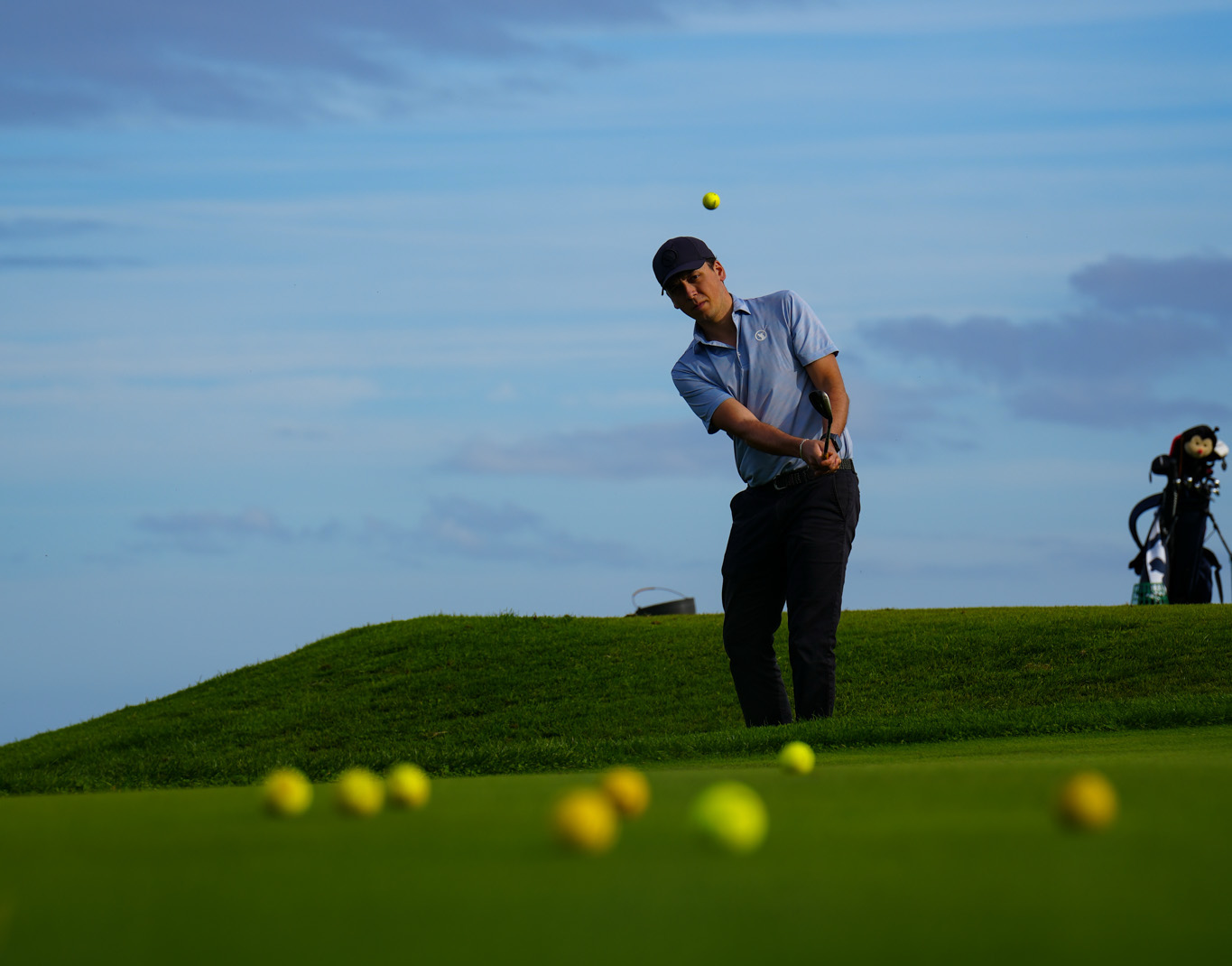 Golfer hitting a chip shot with the ball in the air at dusk