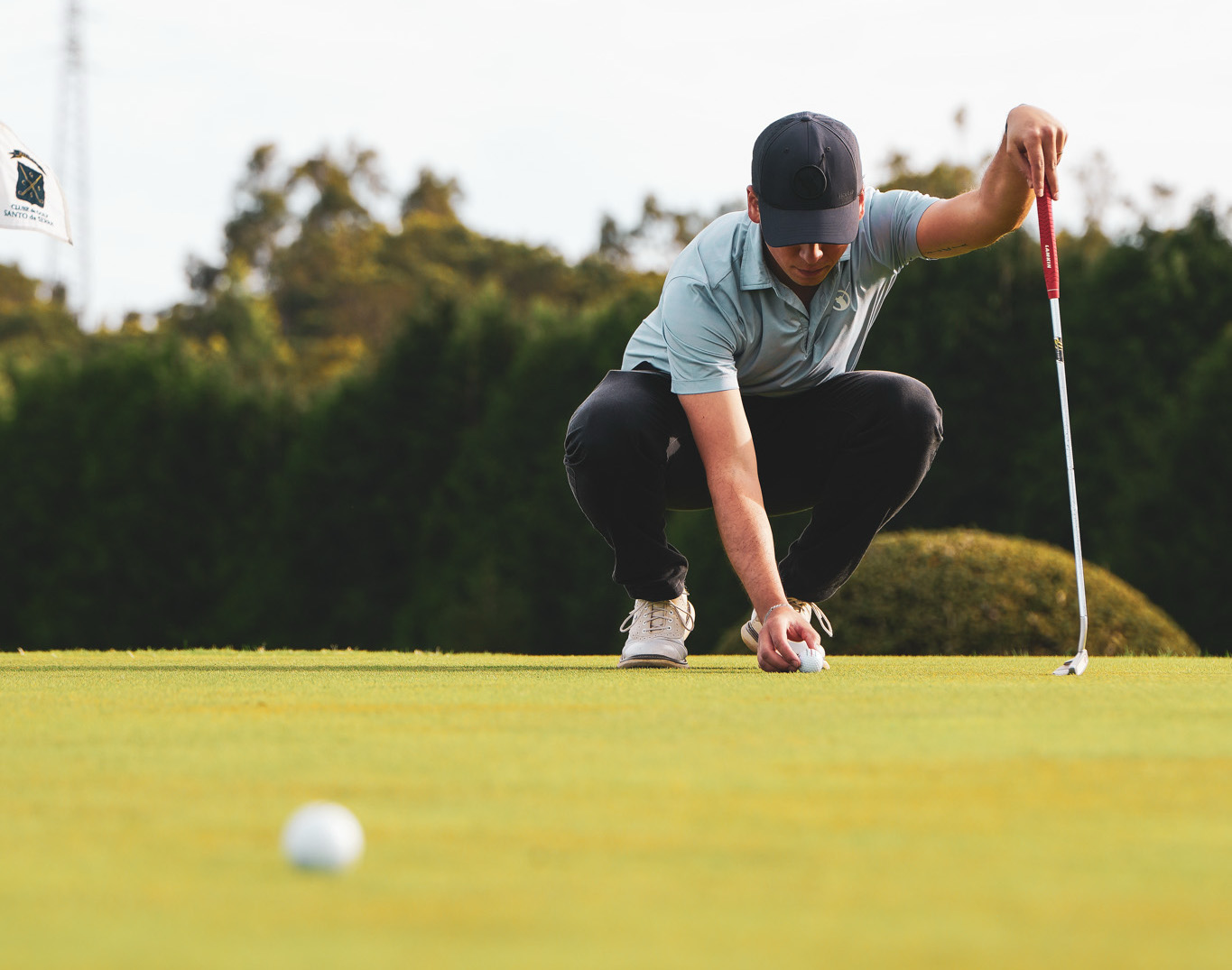 Golfer crouching to line up the ball on the green with a putter