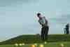 Golfer chipping towards a green with yellow practice balls scattered across the fringe