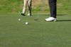 Golfer playing a chip near the green while a playing partner watches