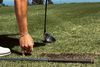 Golfer bending to tee up the ball on a clifftop course (game-improvement)