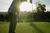 Golfer putting on the green at sunset beside the flagstick