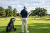 Golfer with a push trolley checking a phone while looking down a tree-lined parkland hole