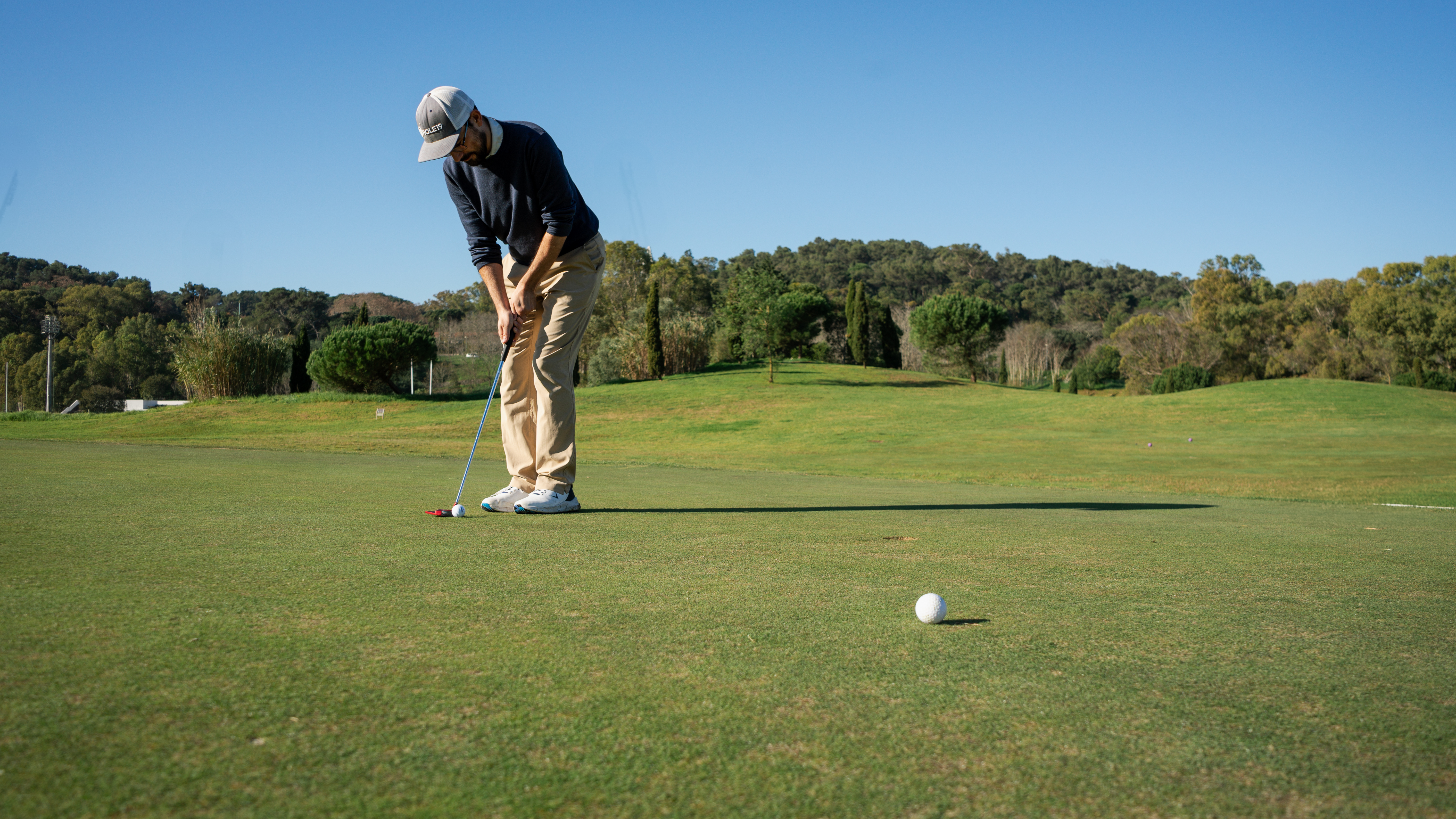Golfer putting on the green with wooded hills behind
