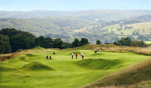 Golfers on an undulating green with rolling hills and open countryside beyond