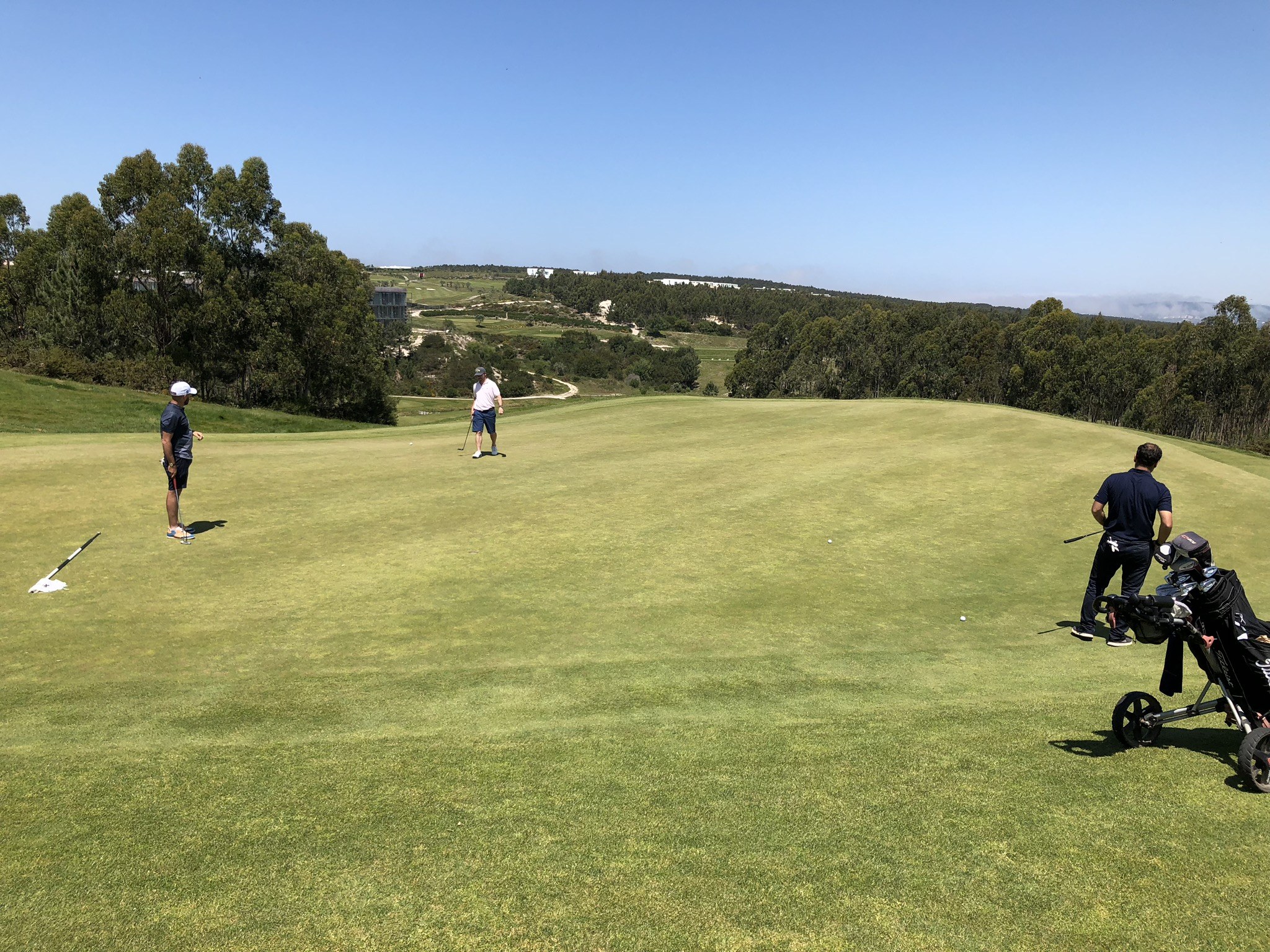 Golfers walking a fairway with trolleys on a sunny day