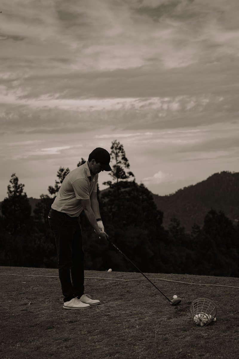 Golfer addressing the ball during a practice swing with mountains behind