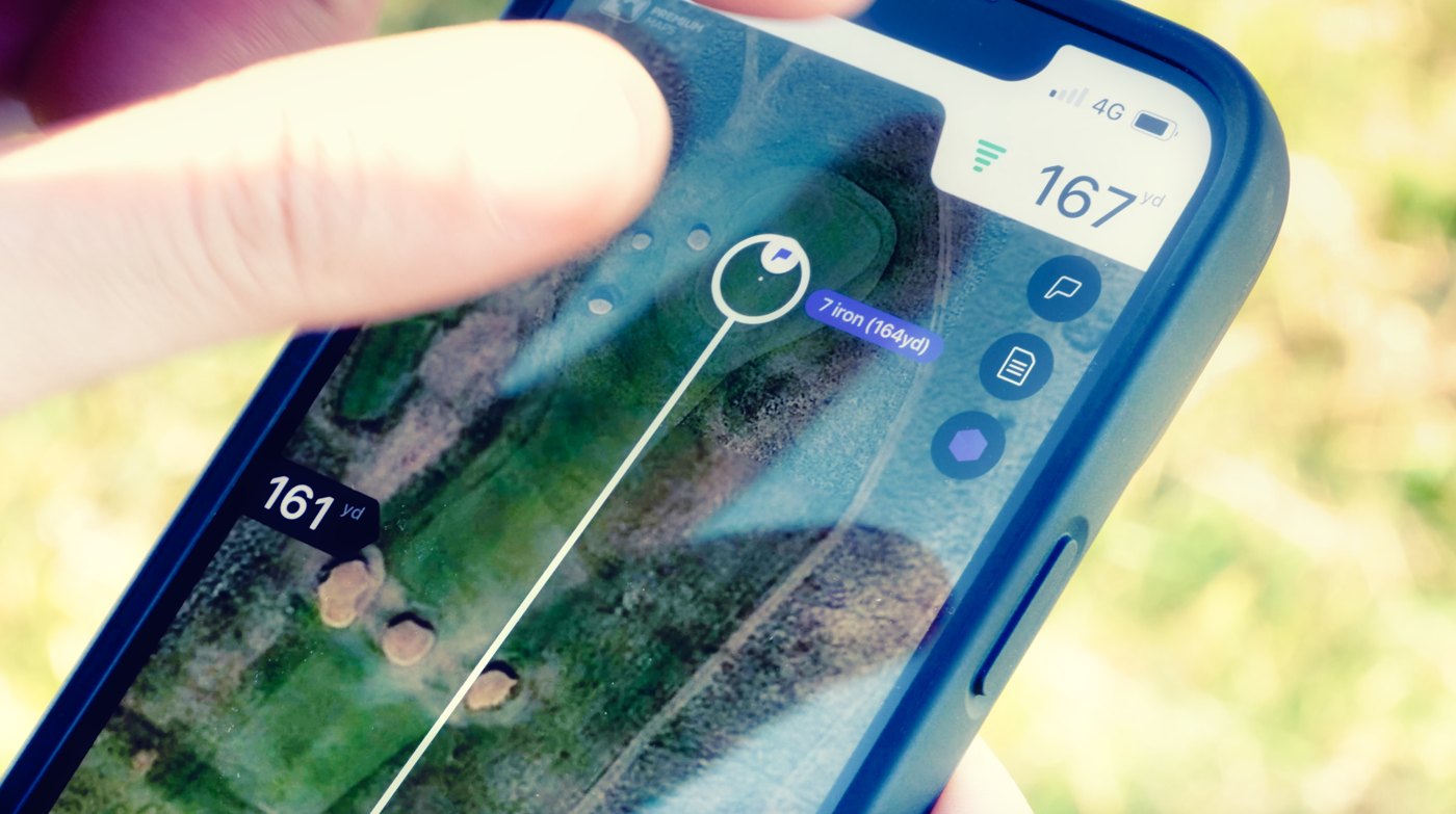 Golfer checking GPS shot distance on a phone during a round