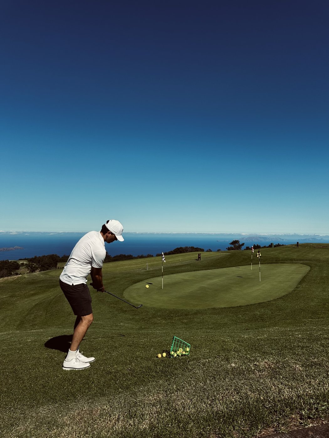 Golfer playing a short chip to a clifftop practice green overlooking the sea (courses)