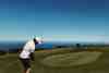 Golfer playing a short chip to a clifftop practice green overlooking the sea (courses)