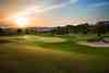 Sunrise over a fairway and bunker with a hilltop clubhouse to one side
