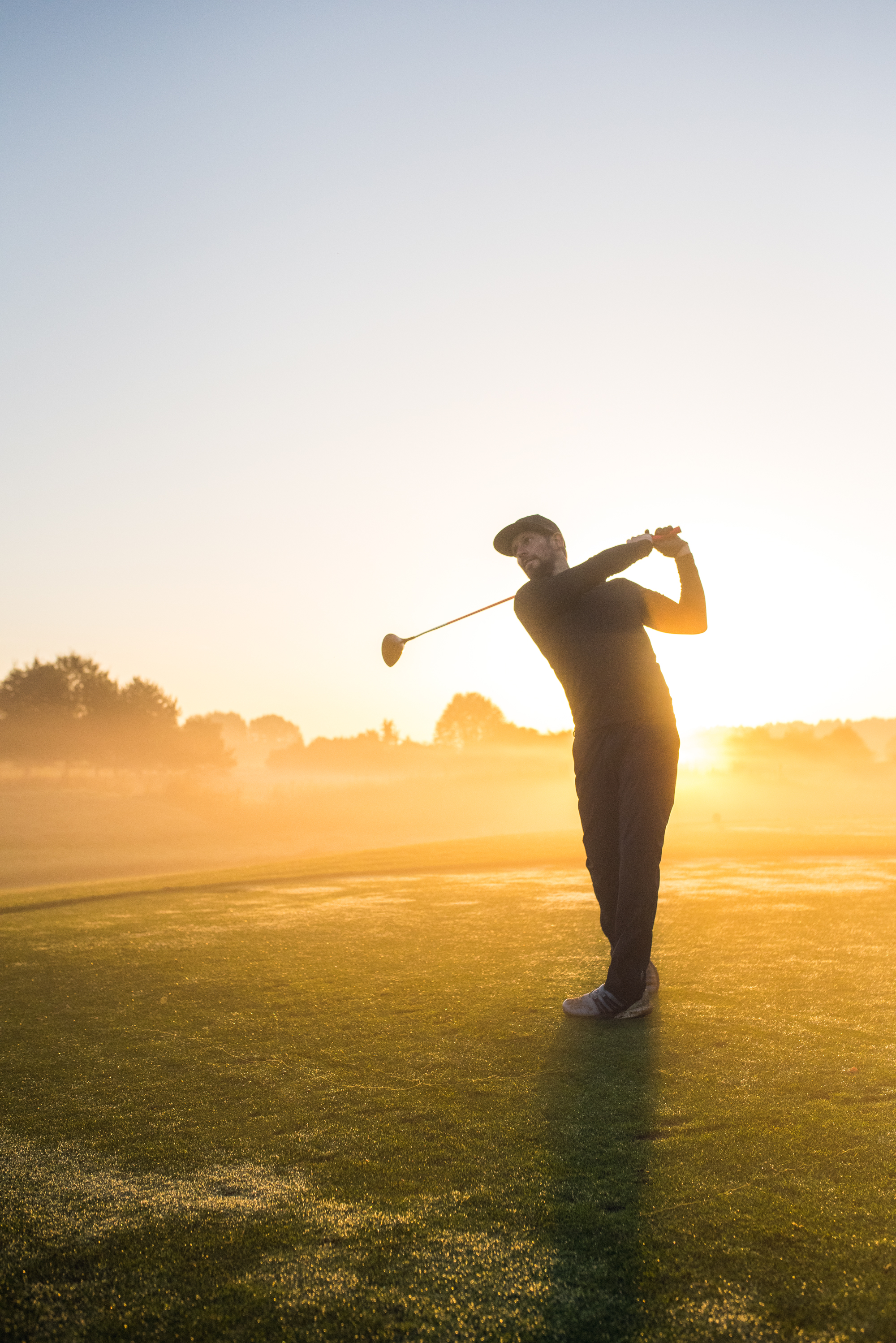Silhouette of a golfer mid-swing in misty light at sunrise