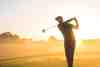 Silhouette of a golfer mid-swing in misty light at sunrise