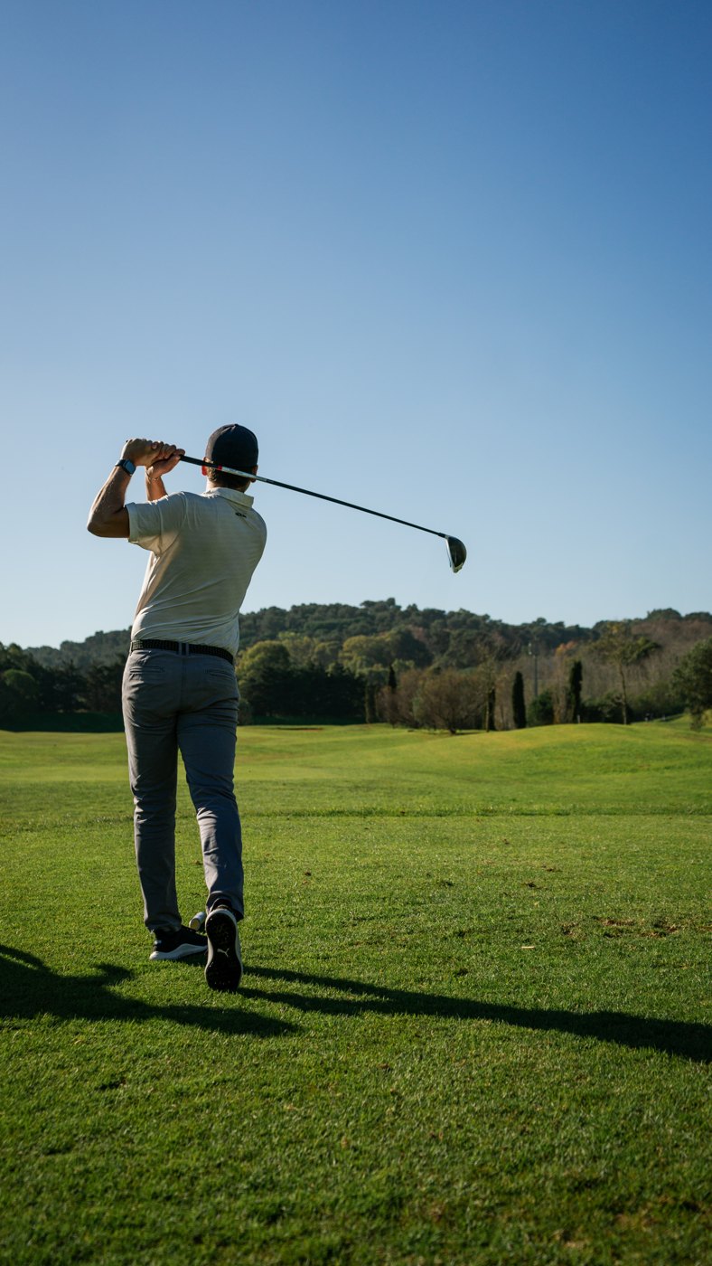 Golfer mid-swing viewed from behind on a fairway