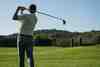Golfer mid-swing viewed from behind on a fairway