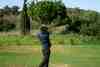 Golfer driving from the tee on a parkland course lined with cypress trees