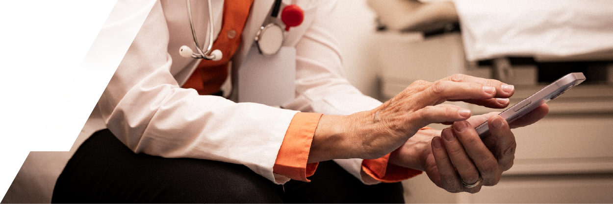 Mid-section view of a doctor wearing a white coat and stethoscope leaning forward typing on his phone
