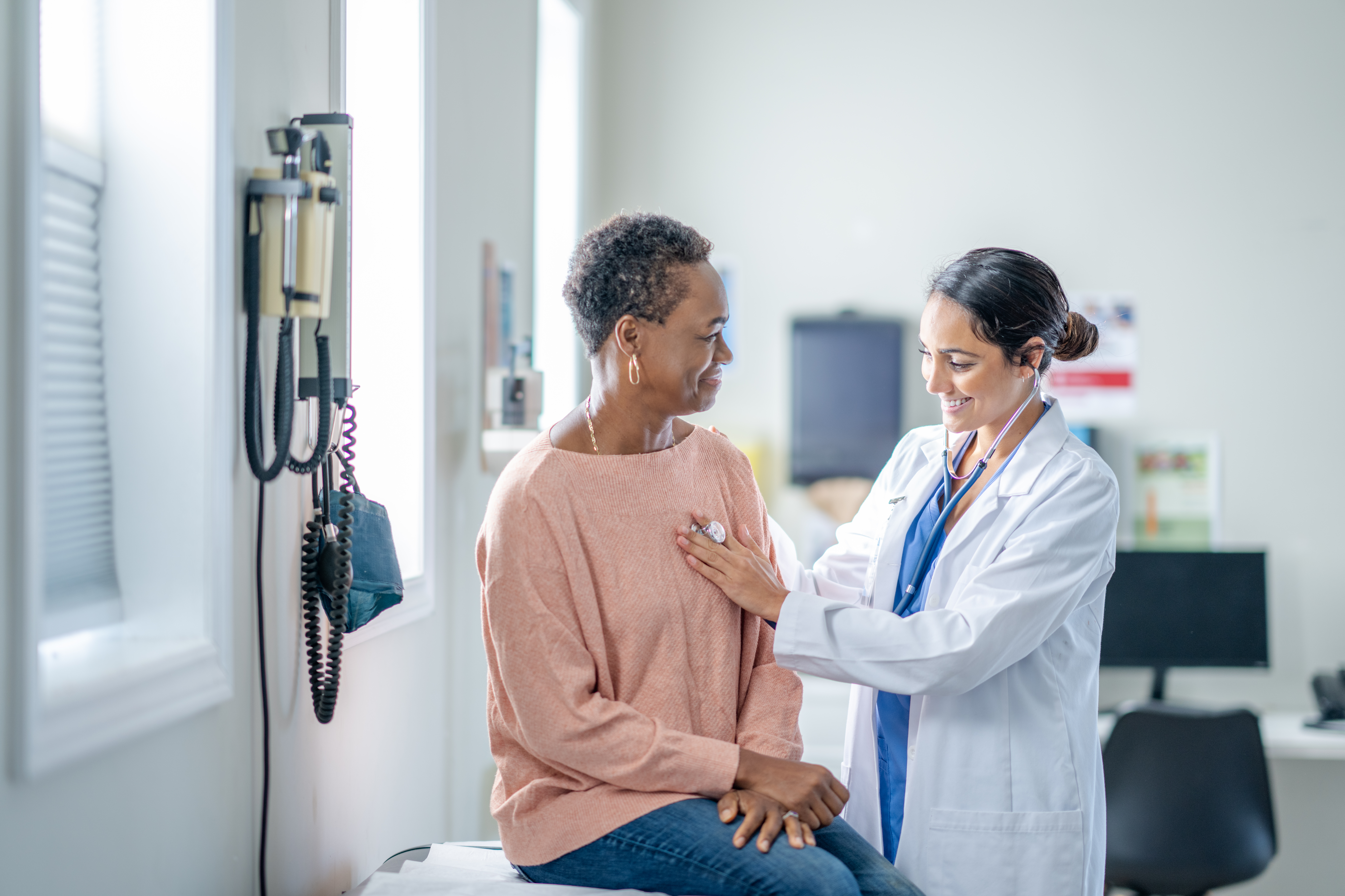 Cardiologist uses stethoscope on patient in medical office