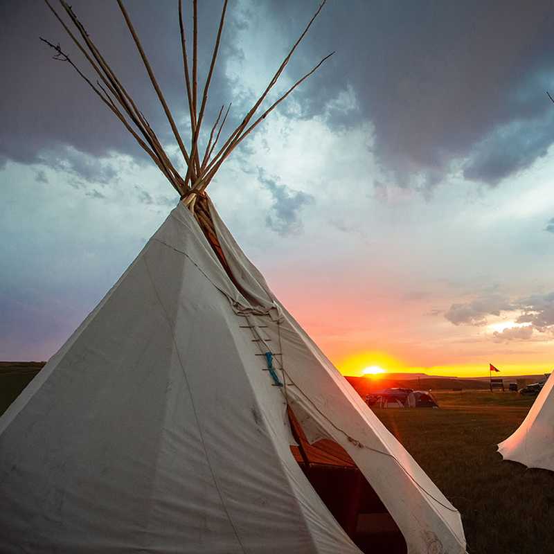 Two canvas tipi tents at sunset on a Montana prairie with dramatic clouds in the sky