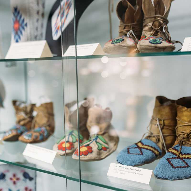 Display case showing beaded and embroidered moccasins and other Native American-style clothing items, likely at a museum or cultural exhibit in Montana