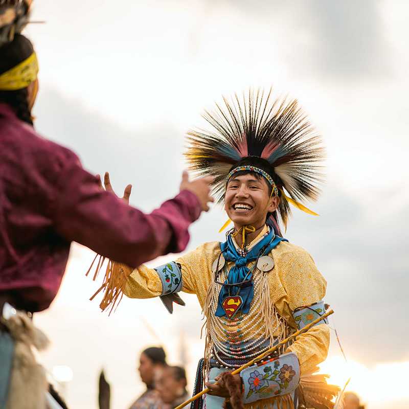 Native American dancer in traditional regalia with feathered bustle during a powwow celebration at sunset