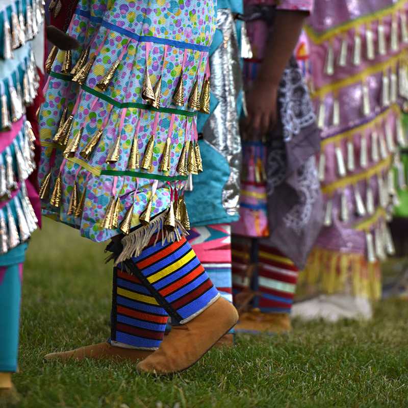 Colorful parade costumes with fringe and ribbon boots standing on grass at a festival