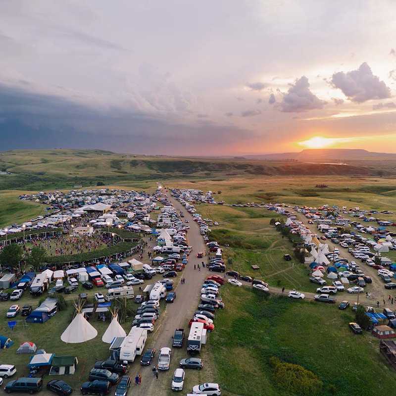 Aerial view of a Montana campground at sunset with rows of RVs and tents along a central road in open green fields