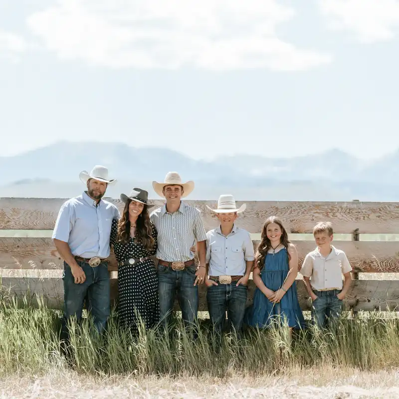 Family posing outdoors in Montana near a stone wall with prairie grass and distant mountains behind them