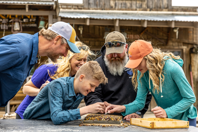 Group of people working together on a jigsaw puzzle at a rustic Montana outdoor gathering with historic buildings in the background