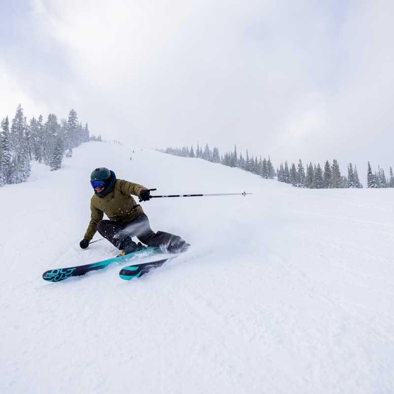 Snowboarder carving through fresh powder on a Montana ski slope with pine-covered mountains in the background