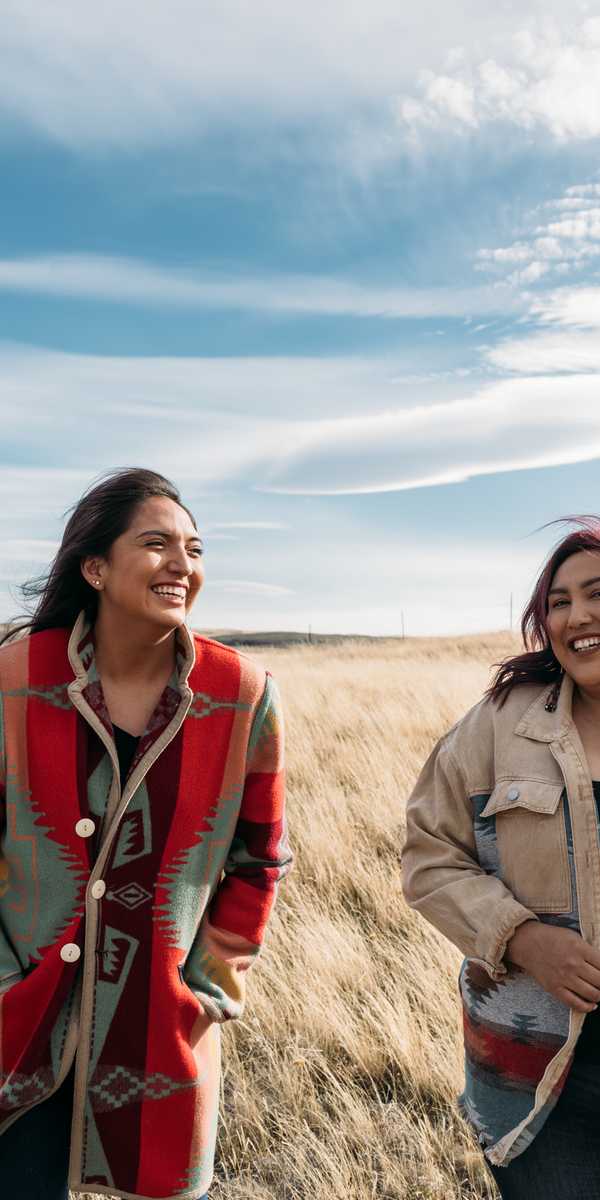 Two people smiling while walking through a grassy field in Montana under a partly cloudy sky
