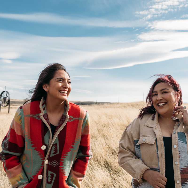 Two people smiling while walking through a grassy field in Montana under a partly cloudy sky