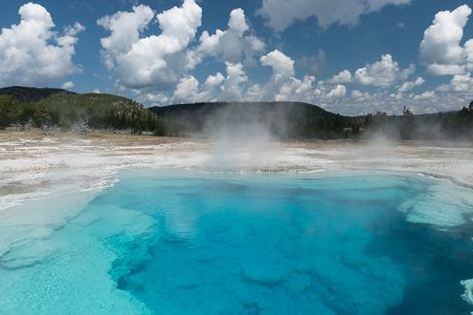 Turquoise geothermal hot spring with steam rising under a cloudy sky in Montana