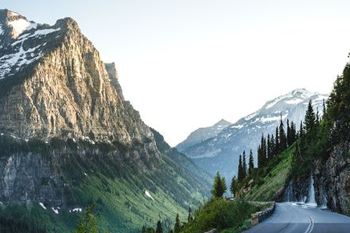 Scenic mountain valley view from a winding road in Montana, with evergreen trees and snowy peaks in the distance