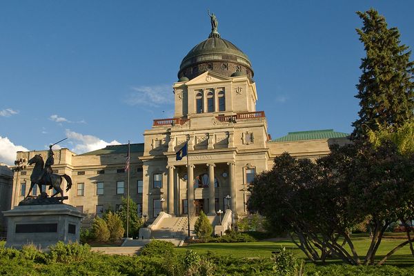 Gold-domed Montana State Capitol building with steps, lawns, and trees under a blue sky