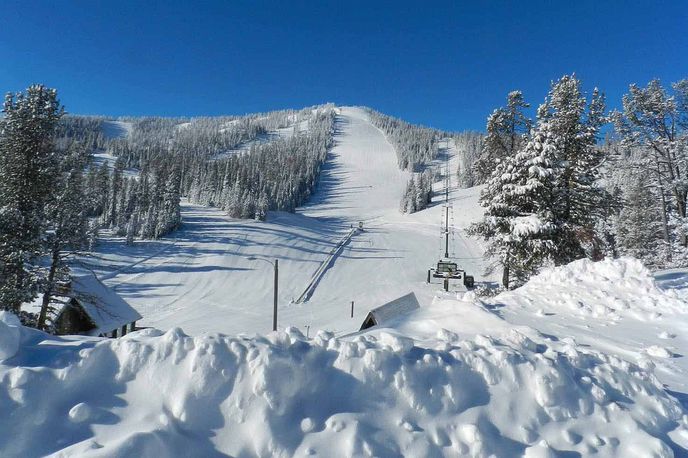 Snow-covered ski slope in Montana with chair lift and pine trees under a clear blue sky