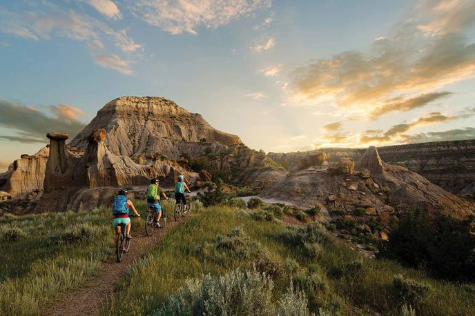 Hikers walk along a trail through Montana’s badlands at sunset near towering rock formations