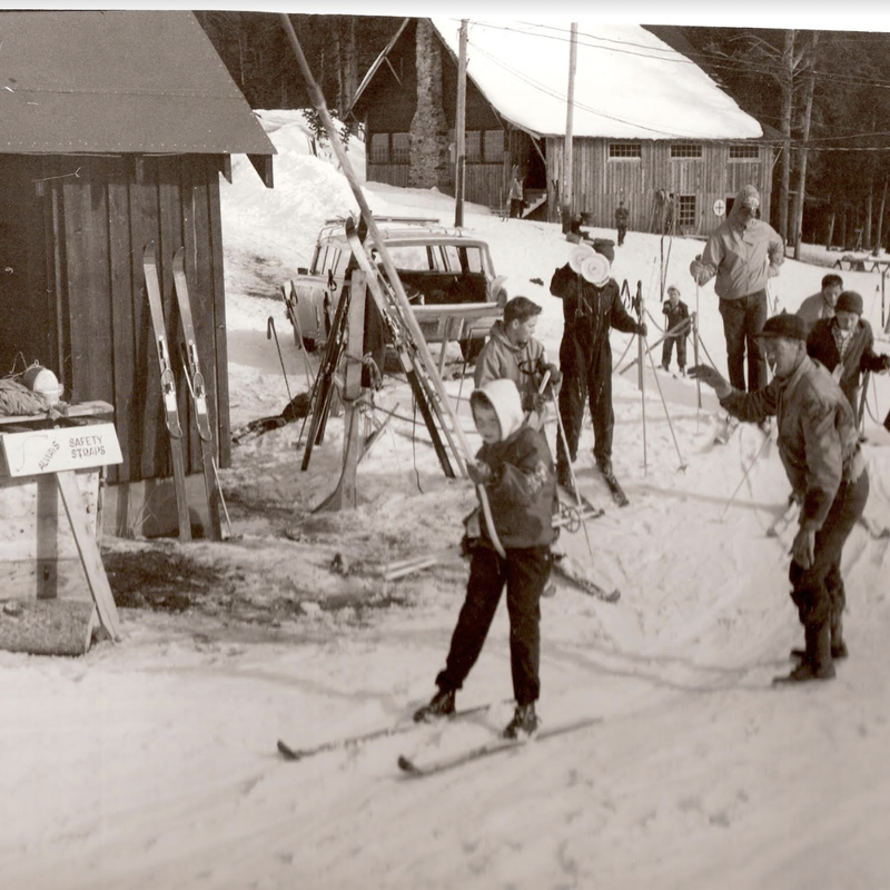 Group walking in snowy street past wooden buildings and equipment in a Montana town during winter