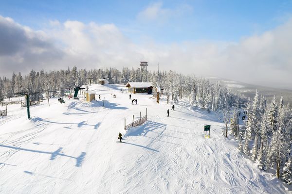 Snow-covered ski trails through a pine forest with chairlifts and resort buildings under a blue sky in Montana