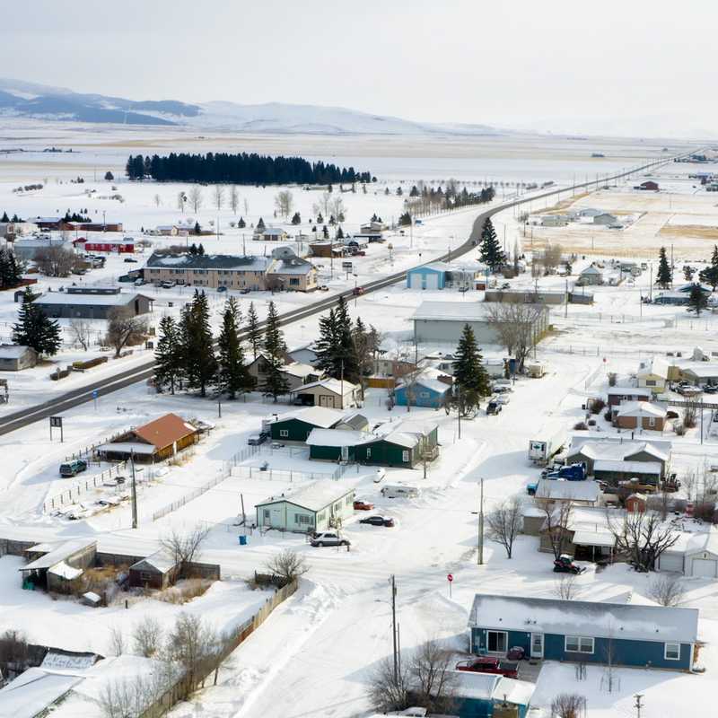 Aerial view of a small Montana town with roads, homes, and snow-covered fields and hills in the distance
