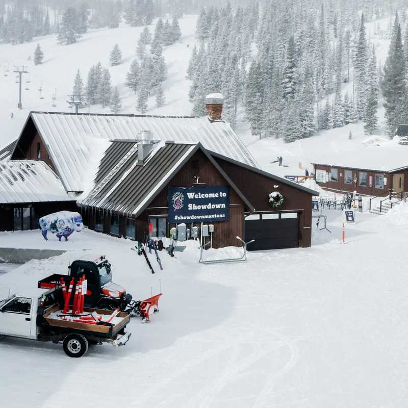 Snowy Montana ski lodge village with groomer equipment and trails through the trees