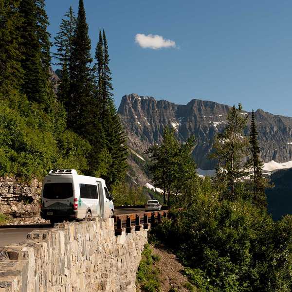White camper van parked along a mountain road with pine trees and a rocky Montana mountain range in the background