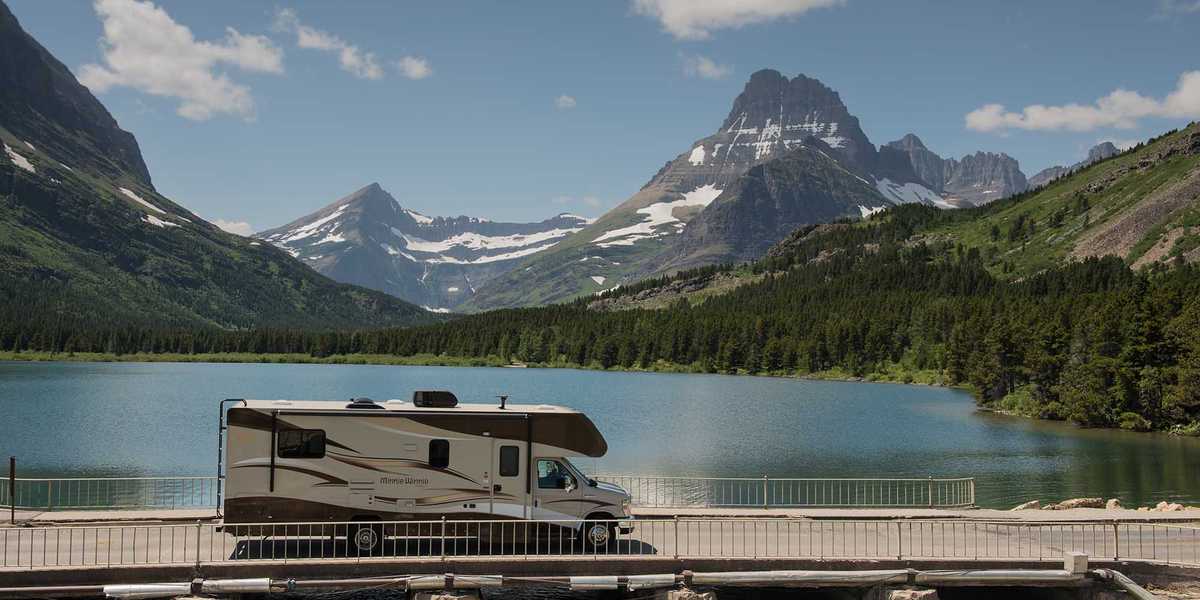 Houseboat docked by a rocky dam on a mountain lake in Montana, with forests and peaks in the background