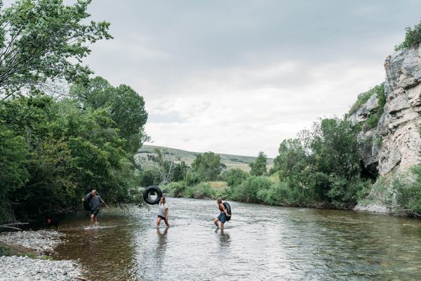 People paddle in a river with cliffs and trees along the Montana shoreline