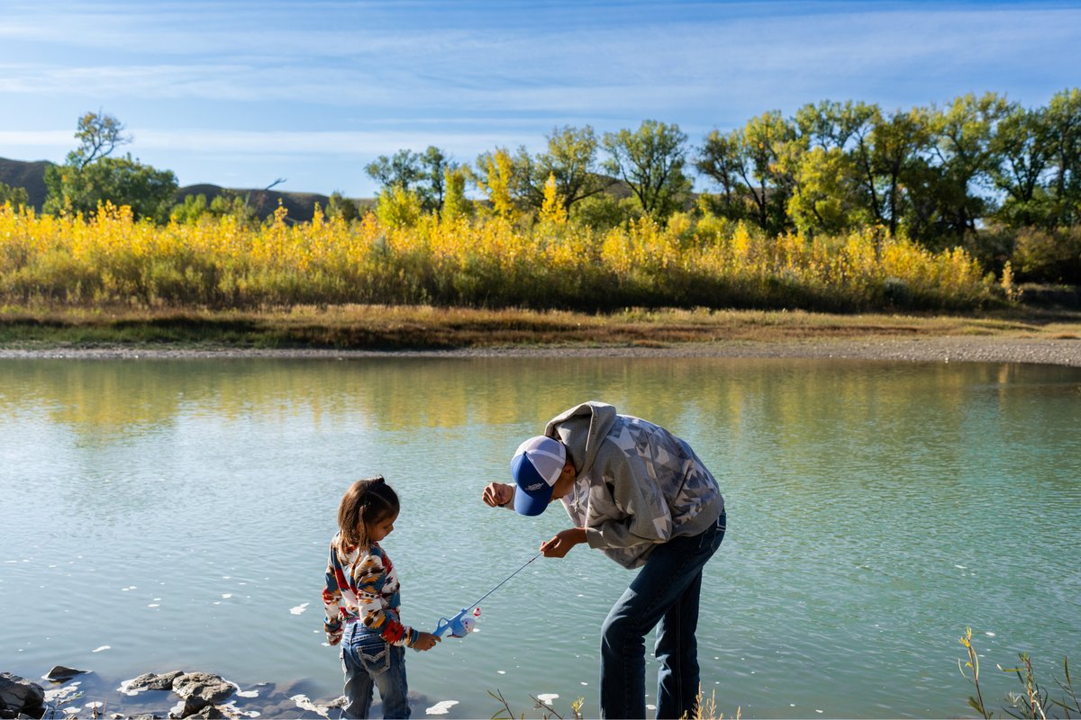 Angler fishing with a child on the shoreline of a Montana lake under a blue sky