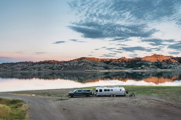 White van parked on a gravel road beside the Missouri River at sunset near a scenic overlook in Montana