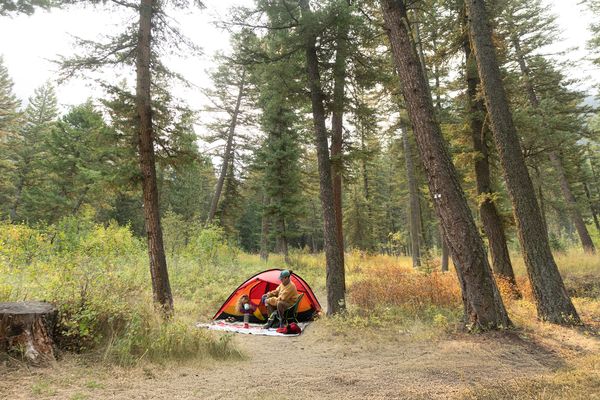 Red tent set up in a forest clearing with a person sitting by the entrance on a camping trip in Montana